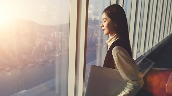 Woman holding laptop while looking out window Woman holding laptop while looking out window